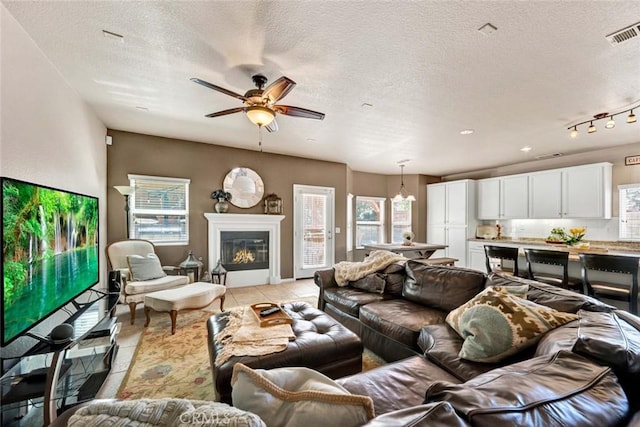 living area featuring light tile patterned flooring, ceiling fan, a textured ceiling, and a glass covered fireplace