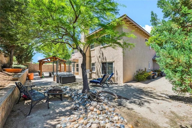 back of house with stucco siding, a gazebo, fence, a patio, and an outdoor living space with a fire pit