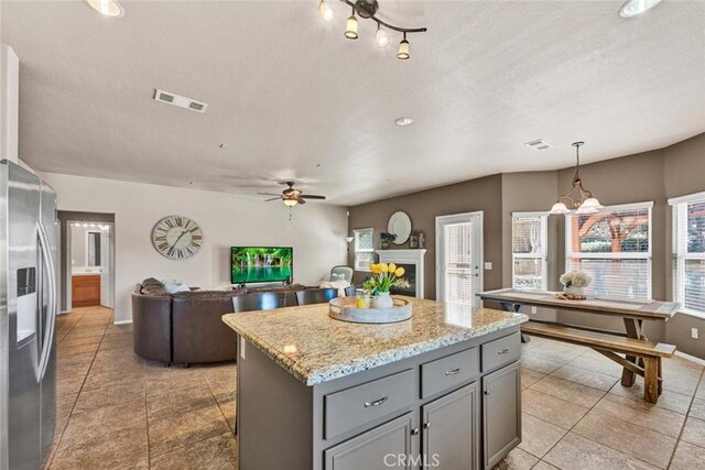 kitchen with stainless steel refrigerator with ice dispenser, gray cabinetry, ceiling fan, a center island, and light tile patterned floors