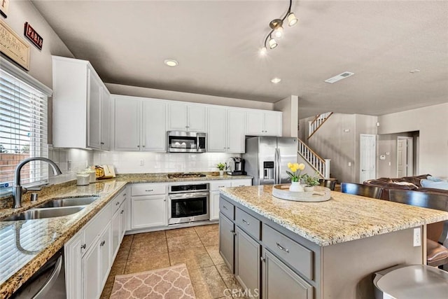 kitchen with stainless steel appliances, a sink, gray cabinetry, decorative backsplash, and white cabinets