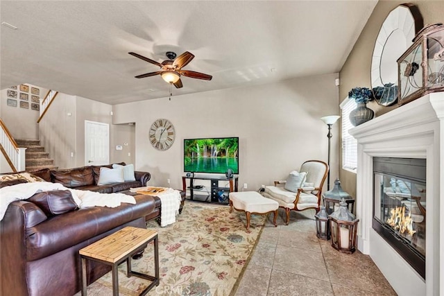 living room featuring a glass covered fireplace, stairway, and ceiling fan