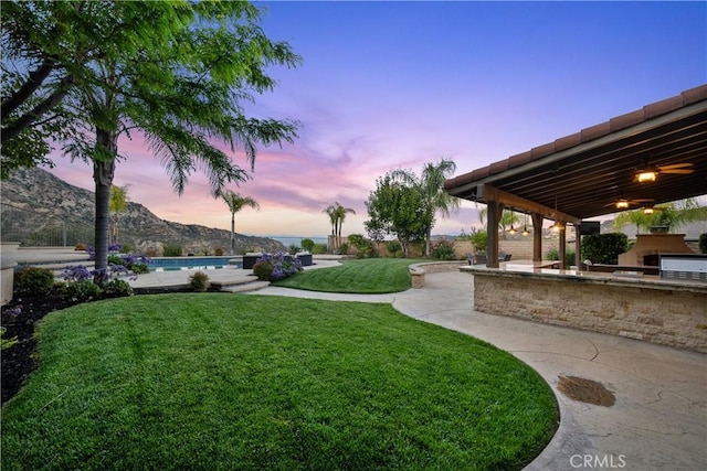 25865 Tulip Grove St, Stevenson Ranch, CA 91381 - yard at dusk with an outdoor kitchen, a lawn, an outdoor pool, a patio area, and a mountain view
