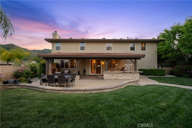 25865 Tulip Grove St, Stevenson Ranch, CA 91381 - back of property at dusk with a patio, a chimney, a yard, stucco siding, and area for grilling