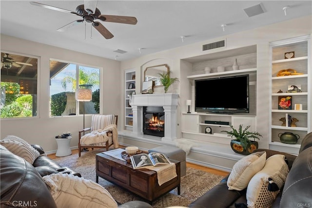 25865 Tulip Grove St, Stevenson Ranch, CA 91381 - living area featuring a ceiling fan, built in shelves, a glass covered fireplace, and wood finished floors