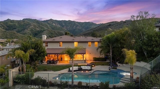 25865 Tulip Grove St, Stevenson Ranch, CA 91381 - back of property at dusk featuring a mountain view, a patio, an outdoor hangout area, a pool with connected hot tub, and stucco siding