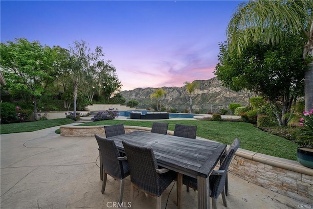 25865 Tulip Grove St, Stevenson Ranch, CA 91381 - patio terrace at dusk featuring a mountain view, a patio area, an infinity pool, a lawn, and outdoor dining space