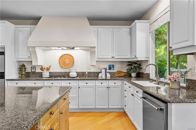 25865 Tulip Grove St, Stevenson Ranch, CA 91381 - kitchen with stainless steel dishwasher, custom range hood, white cabinetry, dark stone countertops, and light wood finished floors