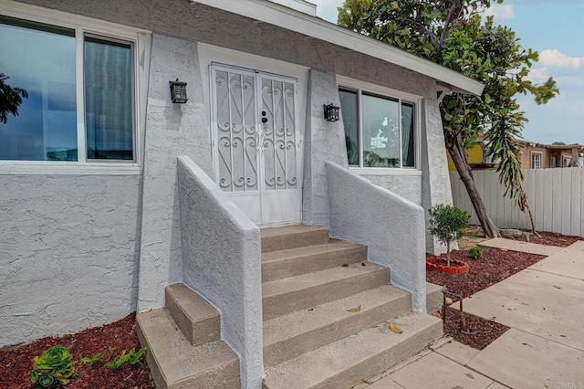 property entrance with stucco siding and fence