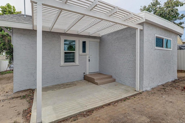 doorway to property featuring stucco siding, a pergola, and a patio area