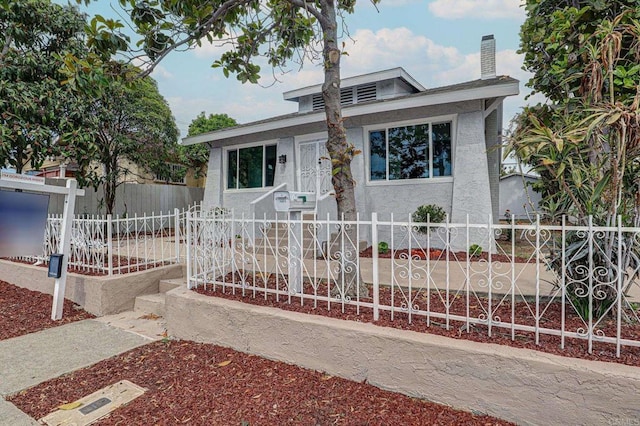 bungalow with a fenced front yard, stucco siding, and a chimney