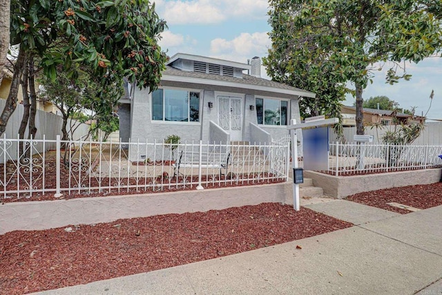 bungalow-style home with a fenced front yard, a shingled roof, and stucco siding