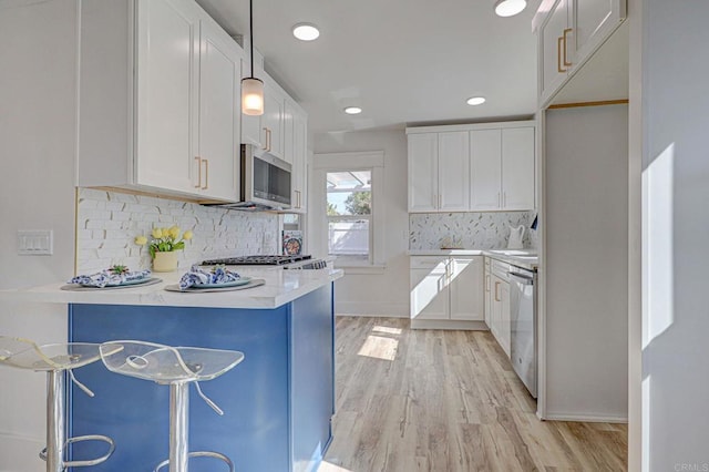 kitchen featuring appliances with stainless steel finishes, a peninsula, light wood-style floors, white cabinets, and recessed lighting