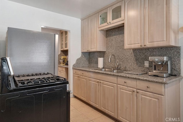 kitchen featuring freestanding refrigerator, a sink, tasteful backsplash, gas range, and glass insert cabinets