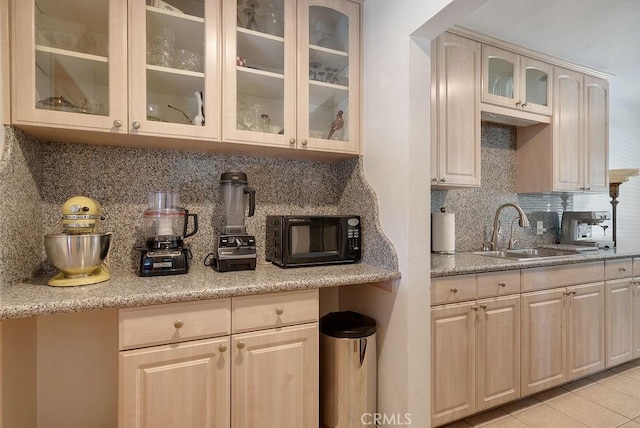 kitchen featuring a sink, black microwave, glass insert cabinets, tasteful backsplash, and light tile patterned floors