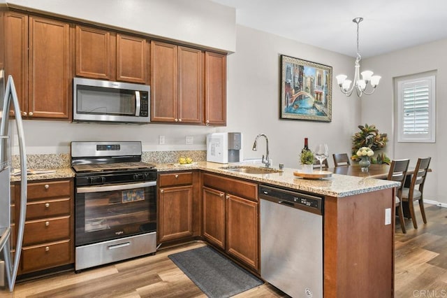 kitchen featuring stainless steel appliances, a sink, a peninsula, light wood-style floors, and brown cabinets