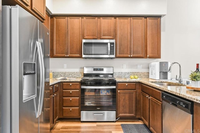 kitchen featuring appliances with stainless steel finishes, a sink, light wood-style flooring, and light stone countertops