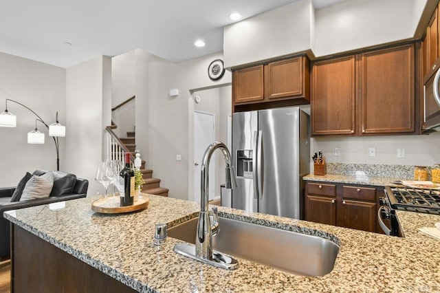 kitchen featuring stainless steel fridge with ice dispenser, a sink, light stone counters, range with gas stovetop, and recessed lighting
