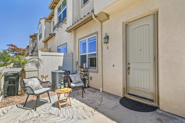 property entrance with fence, central AC, stucco siding, and a patio area