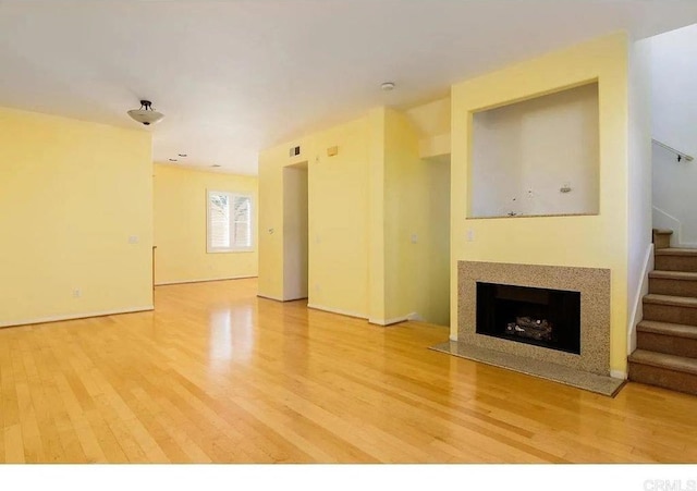 unfurnished living room featuring light wood-style floors, stairway, and a fireplace with flush hearth