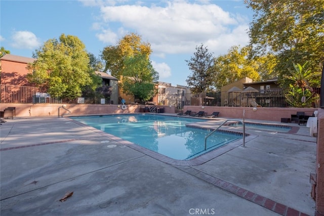 community pool with a patio area, a community hot tub, and fence
