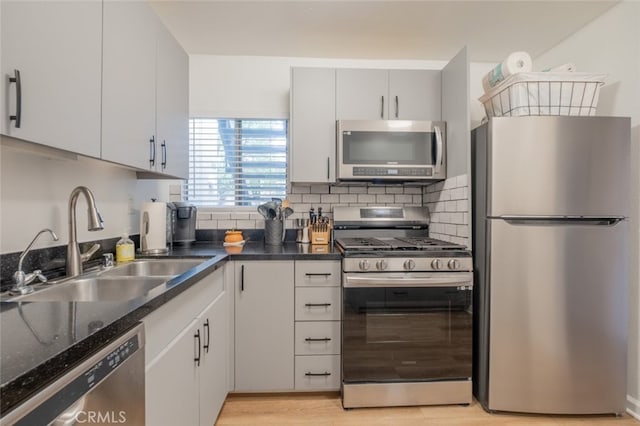 kitchen featuring stainless steel appliances, a sink, backsplash, light wood-style floors, and dark stone counters