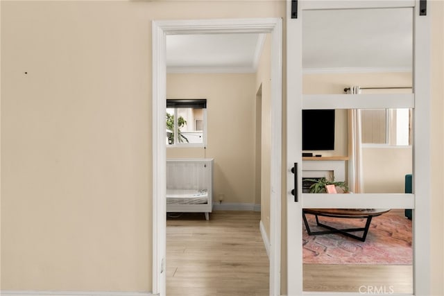 hall featuring crown molding, light wood-style floors, a barn door, and baseboards