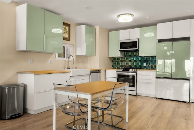 kitchen featuring appliances with stainless steel finishes, a sink, light wood finished floors, decorative backsplash, and white cabinets