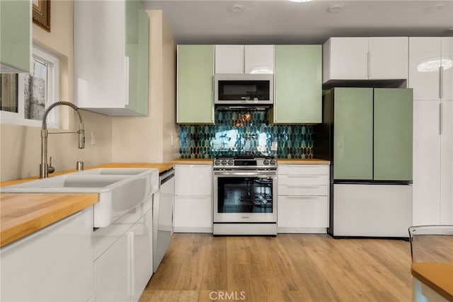 kitchen with stainless steel appliances, a sink, light wood-style flooring, backsplash, and white cabinets