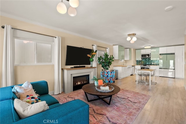living room featuring light wood-style floors, crown molding, and a lit fireplace