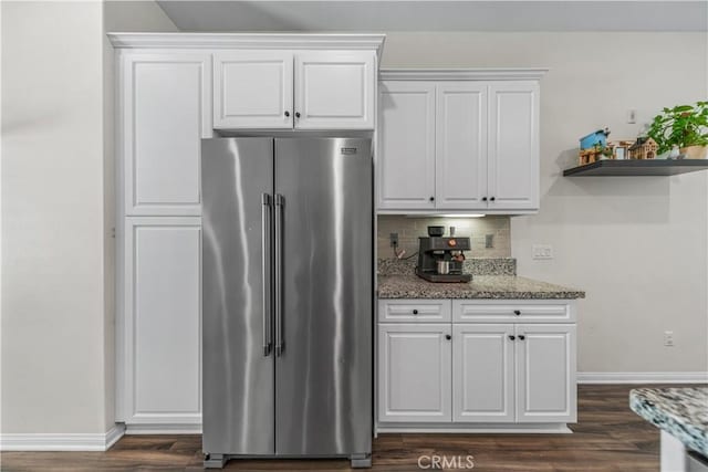 kitchen featuring high end refrigerator, dark wood-style flooring, baseboards, light stone countertops, and tasteful backsplash