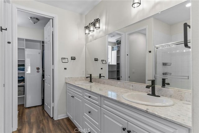 full bath featuring wood finished floors, a walk in closet, a shower stall, double vanity, and baseboards