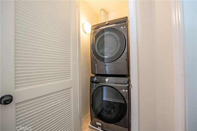 clothes washing area with stacked washer / drying machine and baseboards