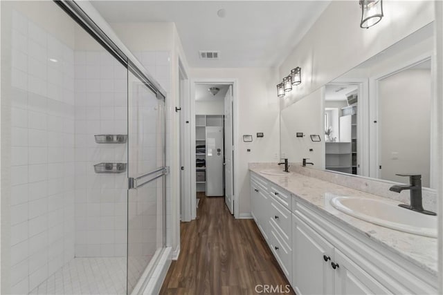 full bath featuring a shower stall, double vanity, wood finished floors, and a walk in closet