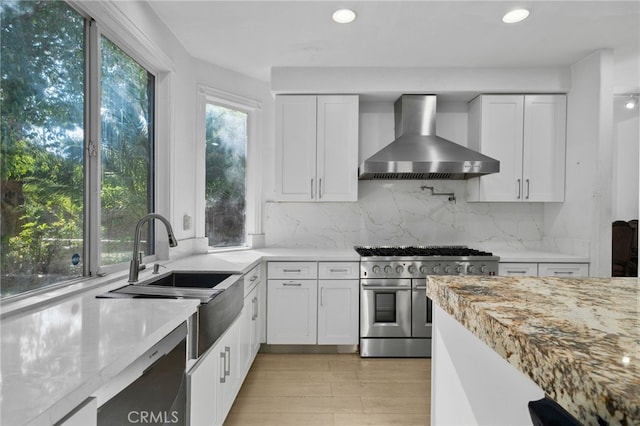 kitchen featuring range with two ovens, wall chimney exhaust hood, a sink, white cabinets, and recessed lighting