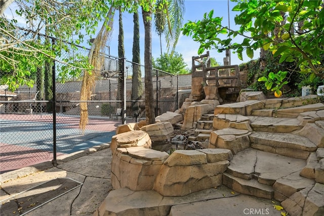 view of property's community featuring a tennis court and fence