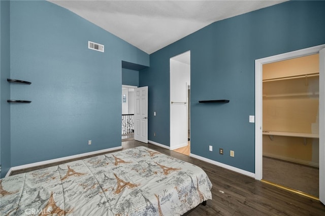 bedroom with vaulted ceiling, wood finished floors, a walk in closet, and baseboards