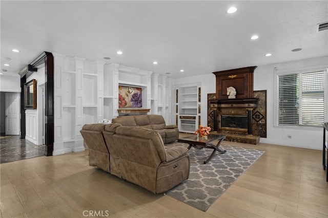 living area with light wood finished floors, a stone fireplace, recessed lighting, and built in features