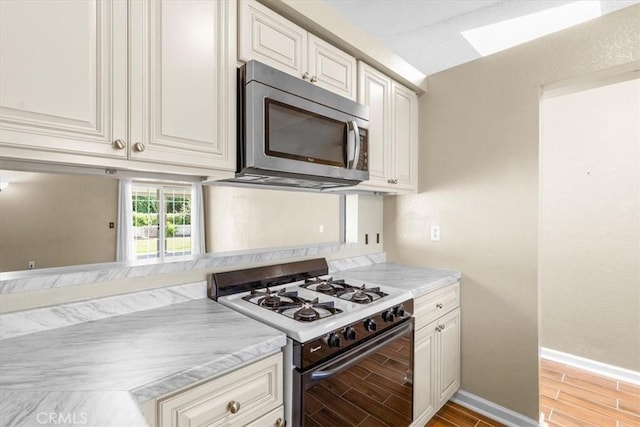 1866 Overland St, Colton, CA 92324 - kitchen with white range with gas stovetop, stainless steel microwave, wood tiled floors, light countertops, and a skylight