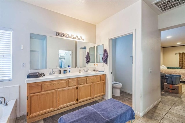 bathroom with tile patterned floors, tiled tub, double vanity, and toilet