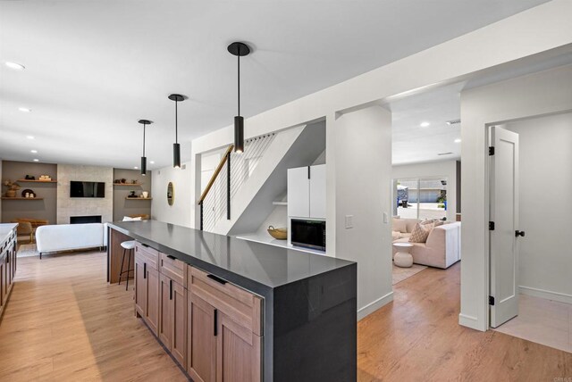 4687 Murat Ct, San Diego, CA 92117 - kitchen featuring open floor plan, dark countertops, light wood-style flooring, a fireplace, and hanging light fixtures
