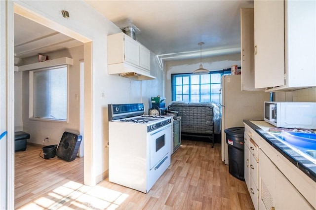 kitchen with white appliances, white cabinetry, light wood finished floors, and decorative light fixtures