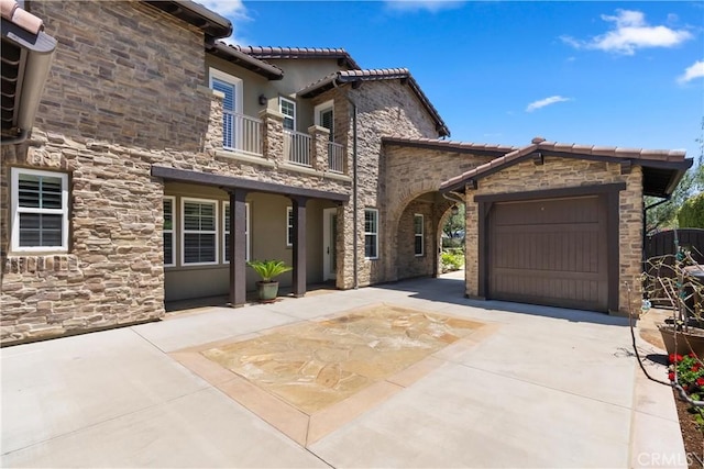 27371 Via Priorato, San Juan Capistrano, CA 92675 - view of front of property featuring a balcony, stone siding, driveway, a tile roof, and a garage