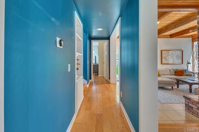 hall with healthy amount of natural light, beamed ceiling, baseboards, and light wood-style floors