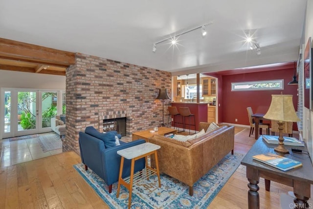 living area featuring beam ceiling, hardwood / wood-style flooring, a brick fireplace, and track lighting