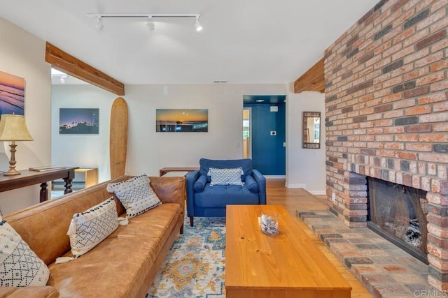 living area featuring rail lighting, a brick fireplace, beam ceiling, and baseboards