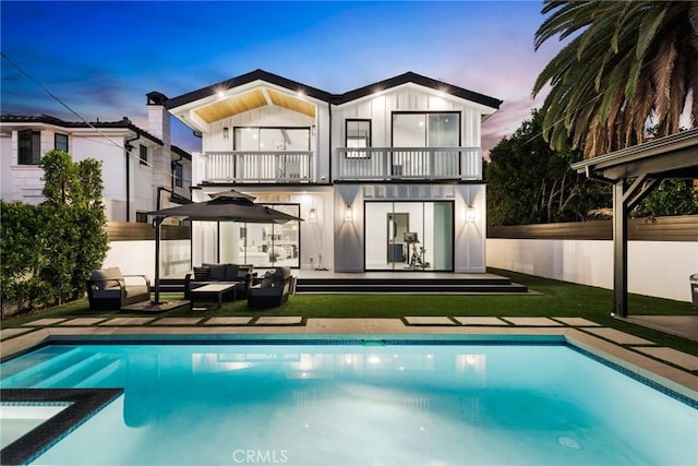 535 N Sierra Bonita Ave, Los Angeles, CA 90036 - back of house at dusk featuring a balcony, an outdoor living space, a patio, board and batten siding, and a pool with connected hot tub