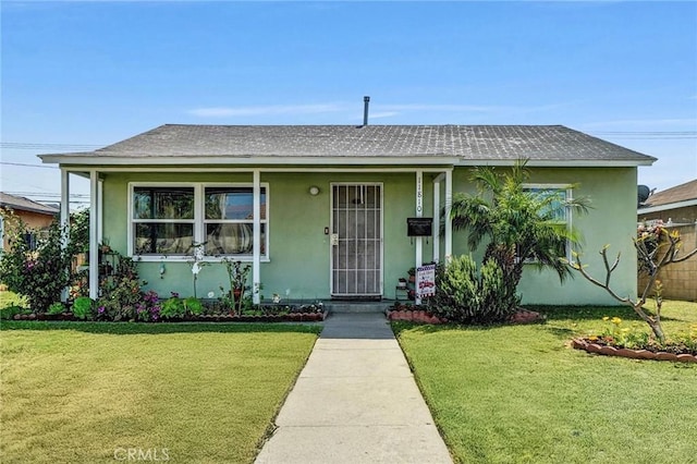 view of front of house featuring stucco siding, a front yard, and roof with shingles