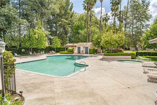community pool with a patio, view of scattered trees, and fence