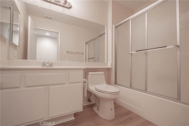 bathroom with toilet, wood finished floors, shower / bath combination with glass door, and vanity