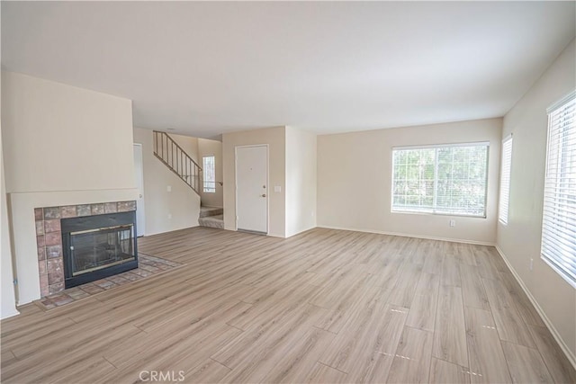 unfurnished living room featuring light wood finished floors, stairs, a tile fireplace, and baseboards